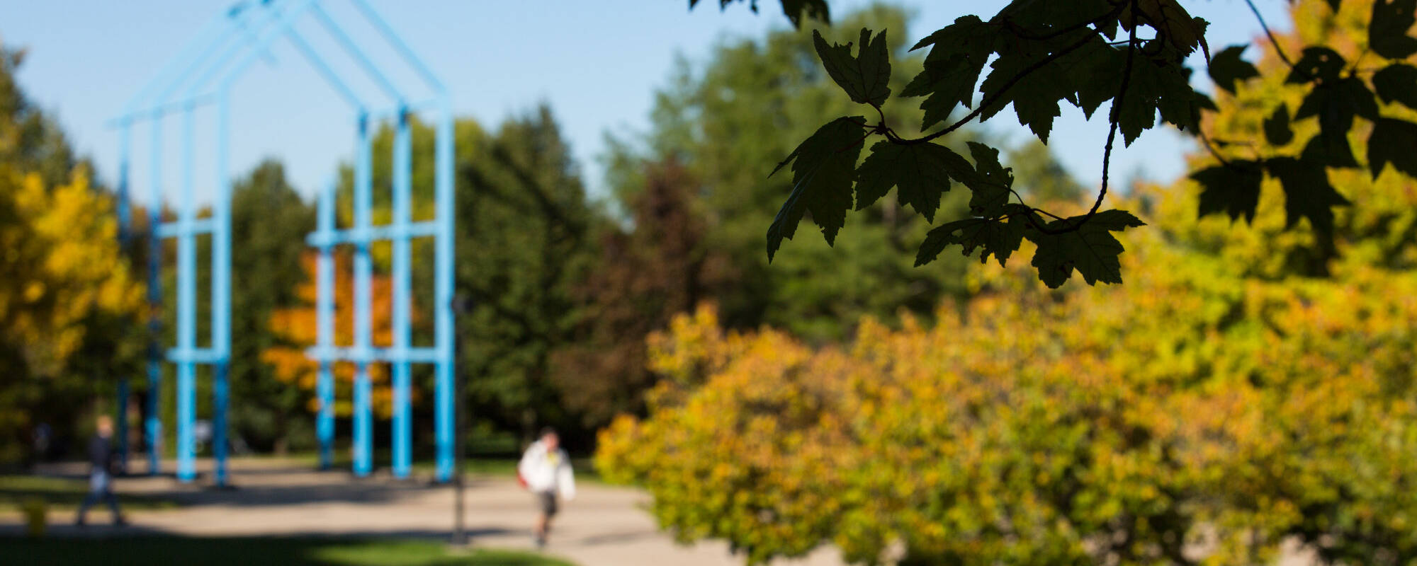 Blue statue on Grand Valley State University's campus framed by vibrant autumn leaves and colorful bushes, capturing the essence of fall